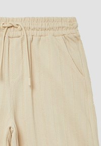 Beige Hose mit Fischgrätmuster, elastischem Bund, Kordelzug und Seitentaschen. Aus weichem, strukturiertem Stoff gefertigt.