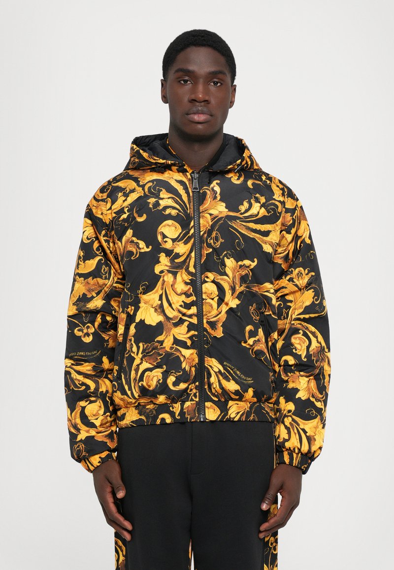 Hooded bomberjacka i svart nylon med intrikata gyllene blommönster, med dragkedja fram och elastiska mudd.