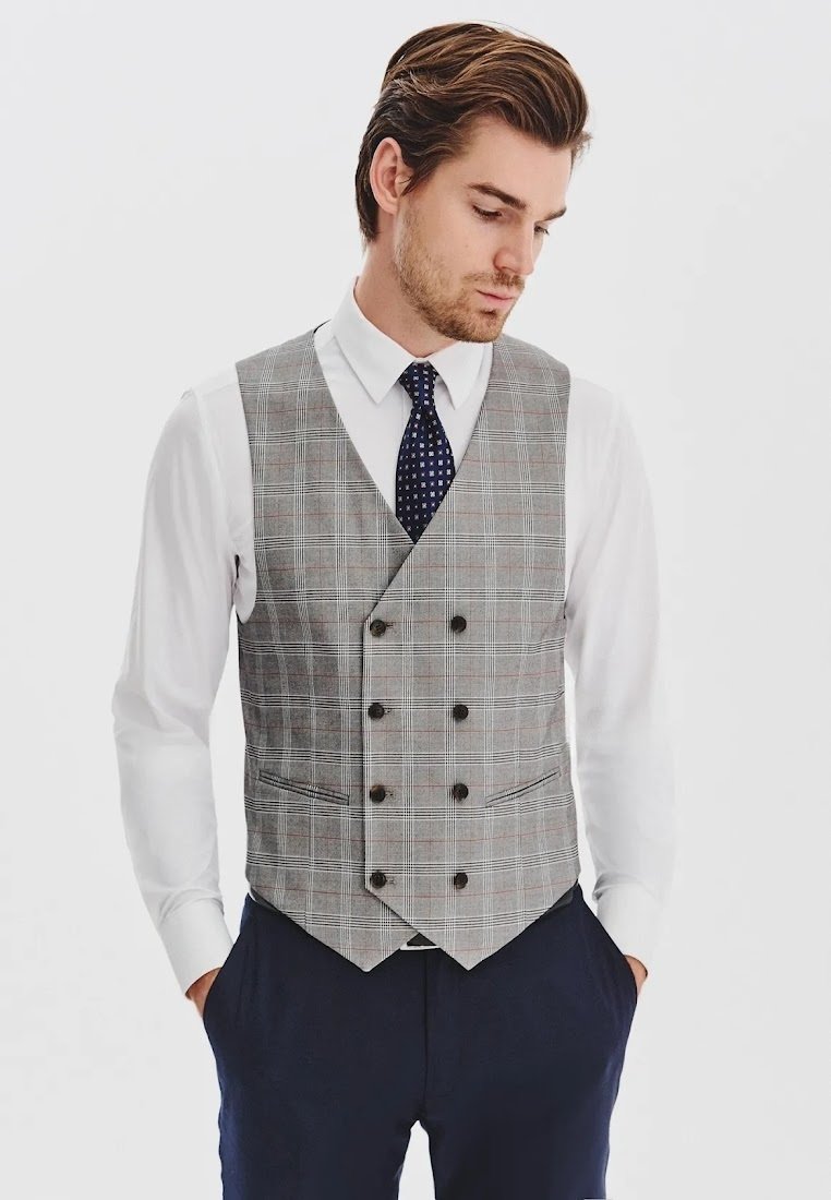 Szary kamizelka w kratę o dopasowanym kroju, z podwójnym zapięciem, sześcioma guzikami i dwoma bocznymi kieszeniami, noszona na białej koszuli.