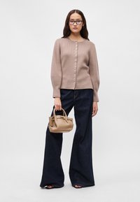 Ανοιχτό καφέ πλεκτό ζακέτα με ραβδωτή υφή, στρογγυλή λαιμόκοψη και κουμπιά από πέρλα, συνδυασμένη με φαρδιά μπλε τζιν και μια μικρή καφέ τσάντα.