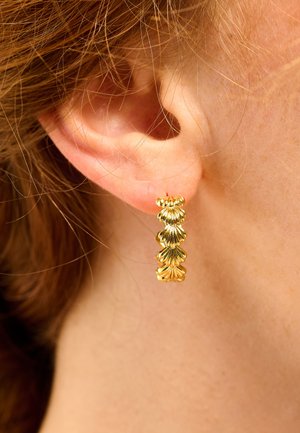 Gold hoop earring featuring scalloped design with textured accents, showcasing a shiny metallic finish against a skin backdrop.