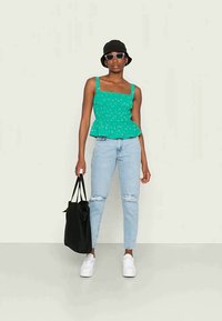 Top peplum verde com pequenos padrões florais, combinado com jeans rasgados azul claro e sapatilhas brancas. Inclui uma bolsa tote preta e um chapéu de balde.