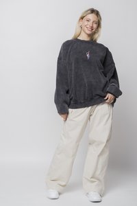 Sömény szürke oversized pulóver hímzett mintával és leengedett vállakkal, krém színű, széles szárú nadrággal és fehér tornacipővel párosítva.