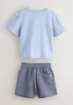 Gaiši zils kokvilnas T-krekls ar īsām piedurknēm, kopā ar pelēkām kokvilnas šortiem, kuros ir elastīga jostasvieta un aizmugurējā kabata.