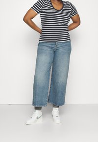 Marineblå og hvide stribede kortærmede V-hals t-shirt parret med brede lyseblå jeans og hvide sneakers med mintgrønne detaljer.