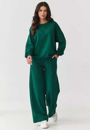 Zielony, oversize'owy sweter z haftowanym napisem, w połączeniu z szerokimi zielonymi spodniami. Wykonany z miękkiego materiału, charakteryzujący się luźnym krojem i elastyczną talią.