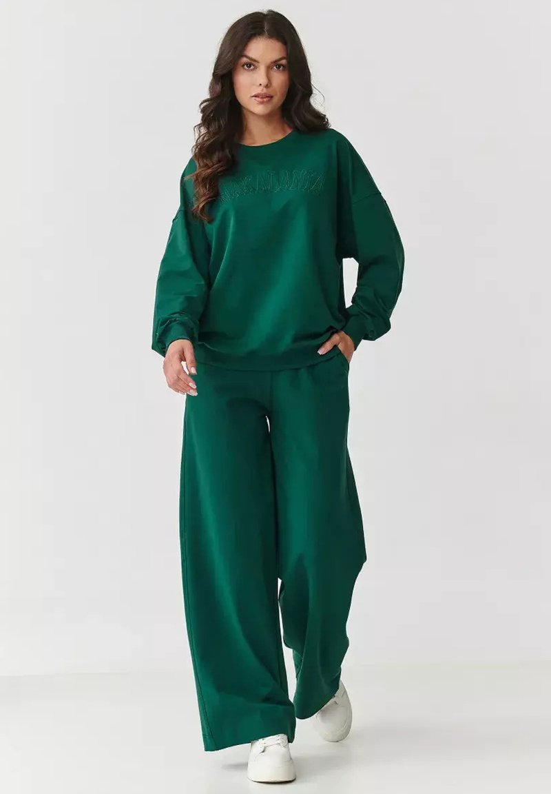 Zielony, oversize'owy sweter z haftowanym napisem, w połączeniu z szerokimi zielonymi spodniami. Wykonany z miękkiego materiału, charakteryzujący się luźnym krojem i elastyczną talią.