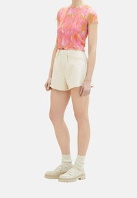 Top de manga corta con un patrón abstracto en tonos rosa y naranja, combinado con pantalones cortos blancos de tiro alto y zapatos de plataforma gruesos en color beige con calcetas.