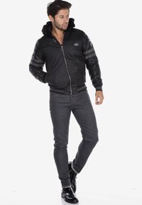 Black bomber jacket with textured paneling, zip closure, and a hood; paired with dark jeans and black ankle boots.