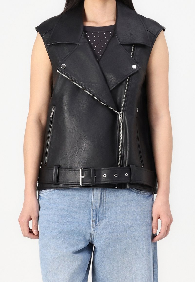 Černá bezrukává motorkářská vesta z umělé kůže s asymetrickým zipem, bočními kapsami a opaskem v pase. Hladká textura se stříbrnými kovovými doplňky.