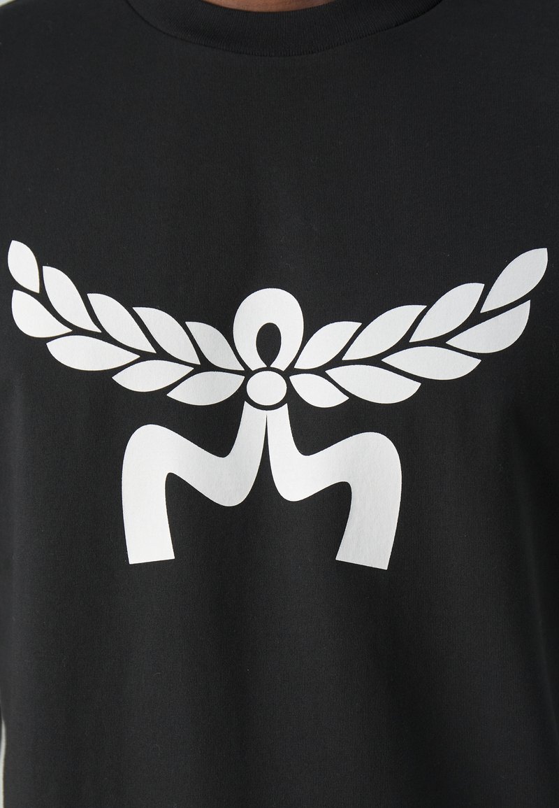 Schwarzes T-Shirt mit einem großen weißen Grafikdesign, das stilisierte Flügel und eine Figur in der Mitte zeigt. Aus Baumwollmaterial, mit Rundhalsausschnitt.