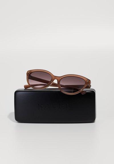 Ochelari de soare ovali maronii cu lentile degradate, așezați pe o carcasă rigidă neagră gravată cu "RALPH RALPH LAUREN." Finisaj neted, mat.