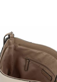 Interior de un bolso beige con un forro de tela suave. Cuenta con un bolsillo con cremallera y un pequeño compartimento de almacenamiento, asegurado con ribete negro.