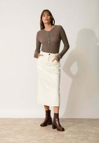 Brązowa, prążkowana bluzka z długim rękawem i guzikami, w połączeniu z kremową midi spódnicą dżinsową oraz ciemnobrązowymi botkami na obcasie.