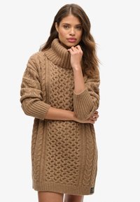 Vestito maglione in maglia color marrone chiaro con collo alto, motivo a trecce testurizzato e maniche a coste. Presenta una toppa con logo sull'orlo.