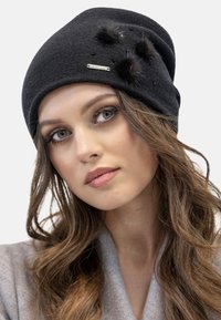 Berretto di maglia nera con pompon in pelliccia e dettaglio metallico, caratterizzato da una superficie texturizzata e una vestibilità aderente.