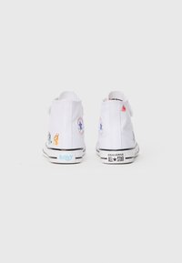 Bijele platnene visoke tenisice s upečatljivim raznobojnim dizajnom likova, crno-bijela gumena potplat i Converse All Star oznaka na peti.