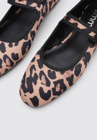 Flachschuhe mit Leopardenmuster und matter Oberfläche, ausgestattet mit einem schwarzen elastischen Riemen und einem runden Zehen-Design, das markante Leopardenflecken hervorhebt.