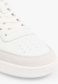 Zapatilla de cuero blanca con una puntera de ante gris, diseño perforado en la punta y suela de goma texturizada blanca. Cordones en color a juego.