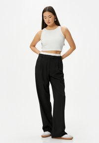 Witte geribde crop top gecombineerd met high-waisted, zwarte wijde broek. De broek heeft een gladde tailleband en een relaxte pasvorm.