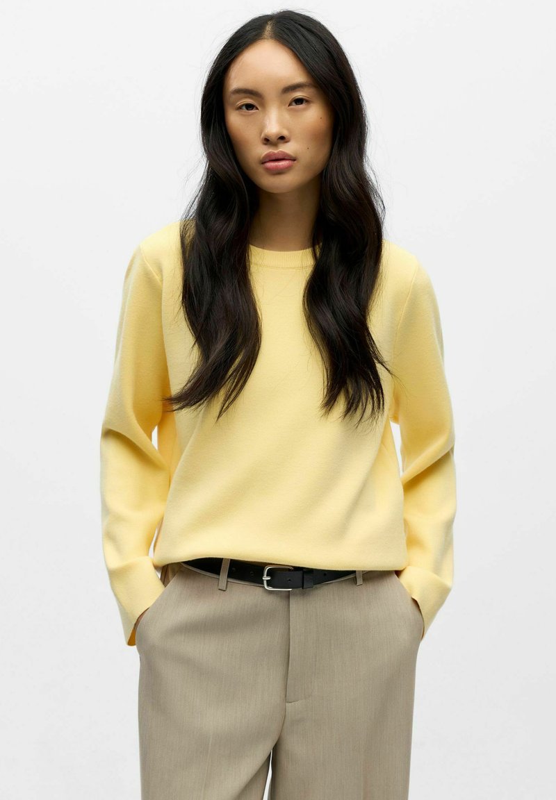 Hele kergelt kollane, pika varrukaga sviiter ümmarguse kaelusega, millele on sobitatud beežid püksid ja must vööt. Sile tekstuur, mugav lõige.