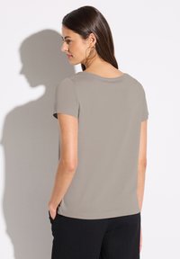 T-shirt à manches courtes, gris clair, avec un col rond, une texture lisse et une coupe décontractée. Mannequin le portant avec un pantalon noir texturé.