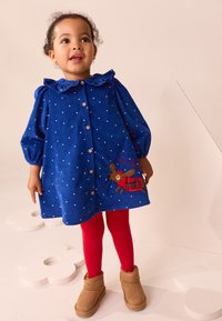 Robe en velours côtelé bleu à pois blancs, col à volants, boutons en bois et renne brodé. Collants rouges et bottes beige complètent la tenue.