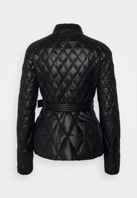 Musta tikattu takki, jossa on korkea kaulus, pitkät hihat ja istuva muotoilu. Siinä on vyö vyötäröllä ja kiiltävä, teksturoitu pinta.