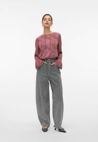 Blusa viola a fantasia con maniche a campana, abbinata a pantaloni a gamba larga a quadri bianco e nero a vita alta e scarpe nere a punta.