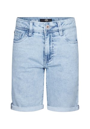 Ung person iført en lys beige t-shirt med et lille logo, oprullede lyseblå denim shorts, hvide sokker med sorte striber og hvide sneakers.