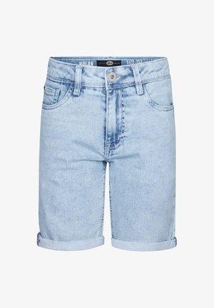 Giovane che indossa una maglietta beige chiaro con un piccolo logo, pantaloni corti in denim azzurro arrotolati, calze bianche con righe nere e sneakers bianche.