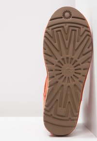 Zapato de ante naranja con una suela de goma texturada que presenta un patrón de rayos de sol y un logotipo en relieve, inclinado para mayor visibilidad.
