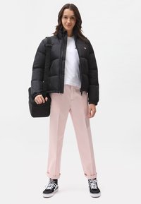 Svart boblejakke, hvit t-skjorte, rosa vide bukser, svart skulderveske, og svarte sneakers med hvite detaljer. Flat bakgrunn.