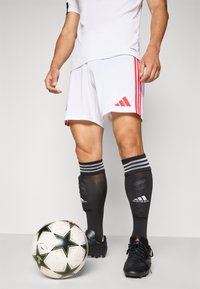 White Adidas shorts with red stripes, black socks with white accents, and black cleats. A patterned black and white soccer ball is nearby.
