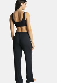 Soutien-gorge de sport noir côtelé avec larges bretelles et bande élastique, associé à un pantalon noir à coupe amples avec une taille élastique.
