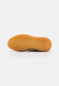 Suola della scarpa con un design di gomma testurizzata caratterizzato da motivi circolari, principalmente in arancione chiaro, con un bordo superiore solido beige.