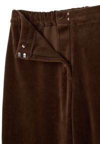 Pantaloni in velluto marrone con una texture liscia, vita elastica, chiusura con bottone e dettagli con zip.