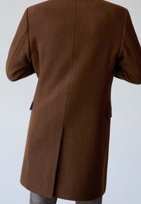 Brown overcoat made of wool blend, featuring a tailored cut, broad shoulders, and a single vent at the back. Includes side pockets.
