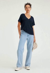 Marinblå t-shirt med v-ringning och kort ärm, kombinerad med ljusblå raka jeans. Modellen håller en beige väska. Avslappnad, lös passform.