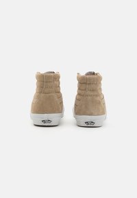 Krémové semišové vysoké tenisky s polstrovaným límcem, bílou gumovou podrážkou a ikonickým logem na patě. Texturovaný povrch se švy.