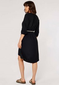 Schwarzes Kleid mit Dreiviertelärmeln, strukturiertem Stoff, tailliert mit einem weißen Gürtel, knielang mit leicht ausgefranster Saumlinie.