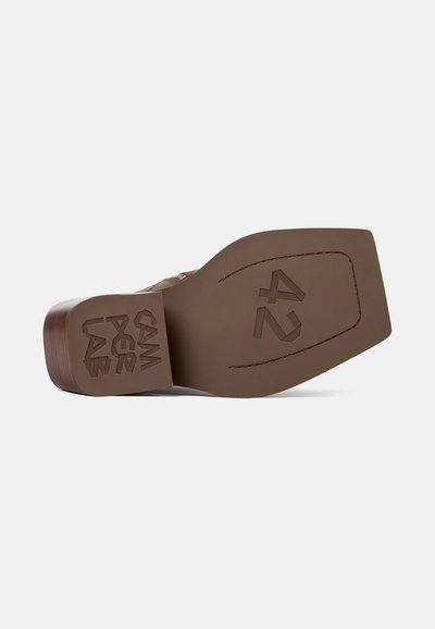Semelle de chaussure marron avec une forme carrée, surface texturée et détails en relief, incluant "42" et des motifs, caractérisée par une construction robuste.