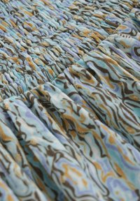 Tissu à motifs bleu, marron et or avec des détails de smock. La texture est froissée avec un aspect doux et léger.