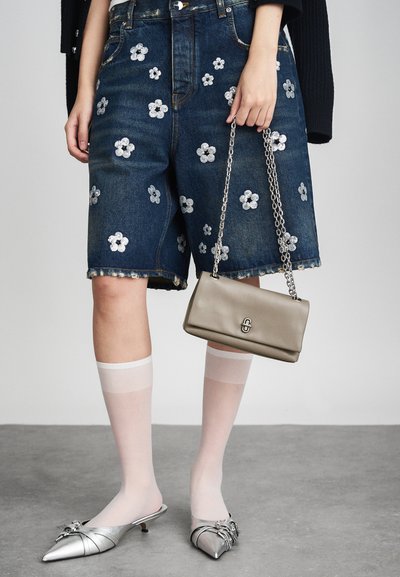Pantalones cortos de mezclilla con adornos florales plateados, combinados con un bolso gris y mule de punta plateada. Se llevan calcetas blancas hasta la rodilla.