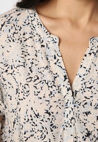 Bluse mit Blumenmuster in hellbeige mit schwarzen und blauen Mustern, mit lockerer Passform, V-Ausschnitt und weichem Stoffgefühl.