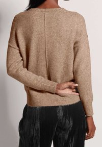 Neulepaita vaaleanruskeana, rento istuvuus, resorit hihansuissa ja helmassa. Hillitty tekstuuri ja laskeutuvat olkapäät, yhdistetty mustiin housuihin.