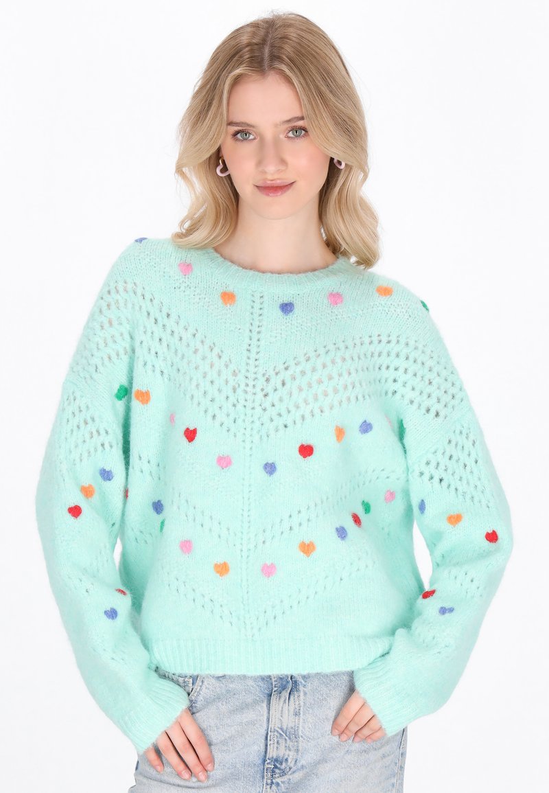 Maglione a maglia verde chiaro con decorazioni multicolori a forma di cuore e motivi a punto aperto. Presenta un collo rotondo e orlo a coste.