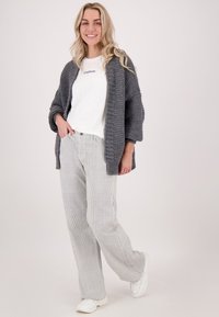 Grijze gebreide cardigan over een witte logo t-shirt, gecombineerd met gestreepte wijde broek en witte sneakers. Soepele textuur, ontspannen pasvorm.