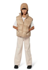 Beige gewatteerde puffer vest met een geometrisch patroon, gecombineerd met een wit T-shirt, beige wijde broek en een bruine gebreide beanie.