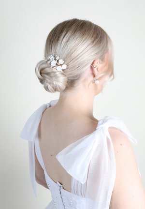 Abito bianco con maniche a fiocco trasparente, schiena decorata e accessorio floreale per i capelli. Capelli acconciati in un basso chignon, con una texture liscia e leggera.